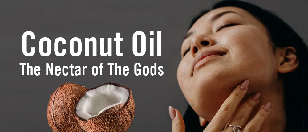 A woman with closed eyes and a content expression applies coconut oil to her neck. Text on the image reads "Coconut Oil: The Nectar of The Gods." An open coconut is shown in the lower left corner against a dark background.