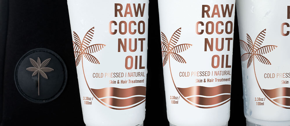 Three white containers of raw coconut oil, labeled for cold-pressed, natural skin and hair treatment, lined up side by side against a dark background.