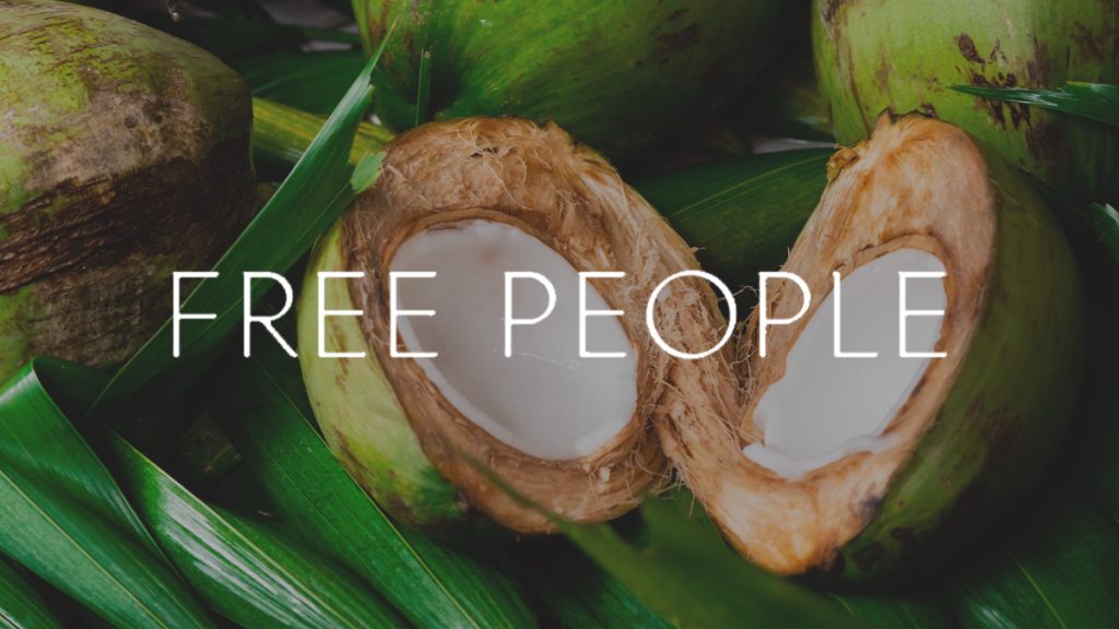 Two fresh coconuts halved and resting on lush green leaves, displaying white coconut meat and clear coconut water, with the text "free people" overlaying the image.