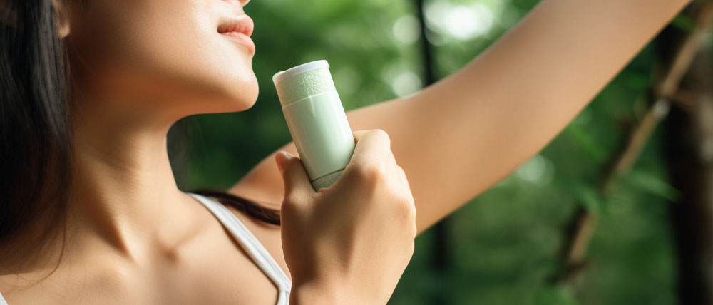 A woman applying deodorant on her underarm in a lush green setting, focusing on the product with a serene expression.