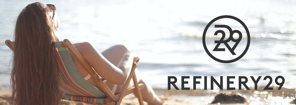 A woman reclining in a beach chair by the ocean, facing away from the viewer, besides the "refinery29" logo on the right.