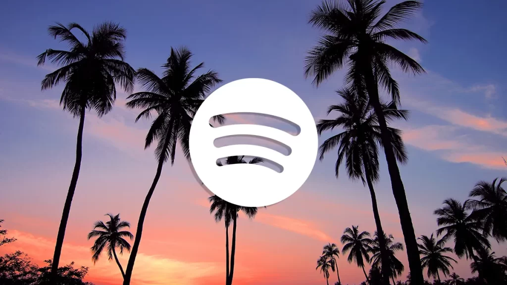 Spotify logo in white centered over silhouettes of palm trees against a colorful sunset sky with shades of pink, purple, and orange.