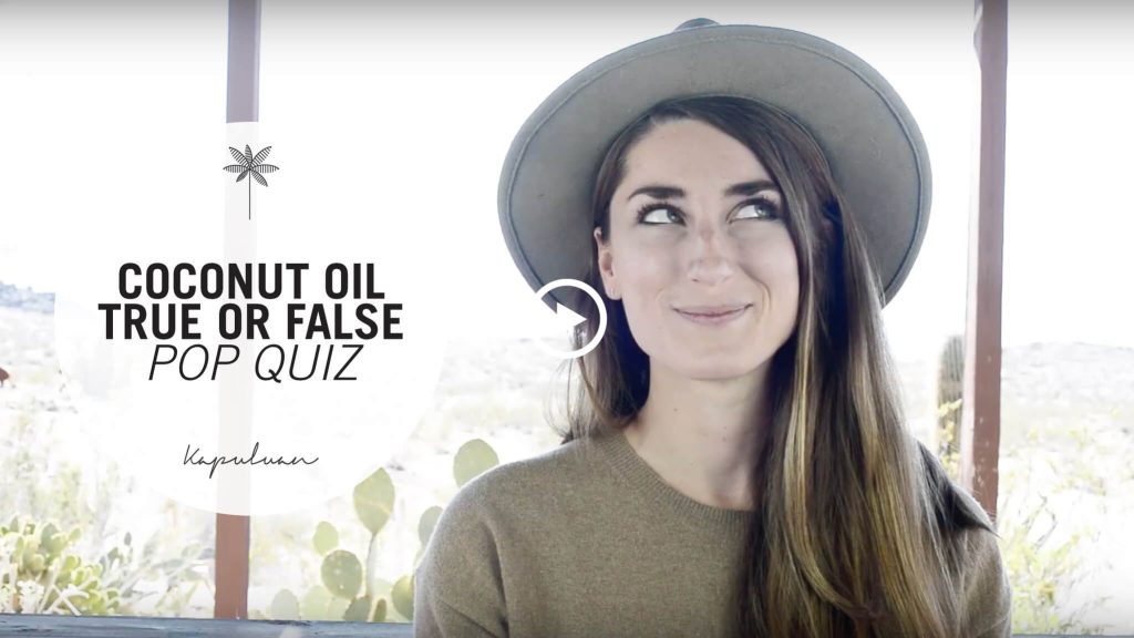 A woman wearing a hat and a smile plays a coconut "true or false pop quiz" against a backdrop of bright windows and greenery.