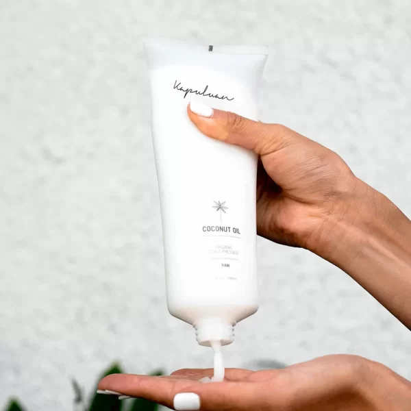 A person holding a tube of Cold Pressed Raw Organic Coconut Oil-infused hand cream, squeezing a small amount onto their finger.