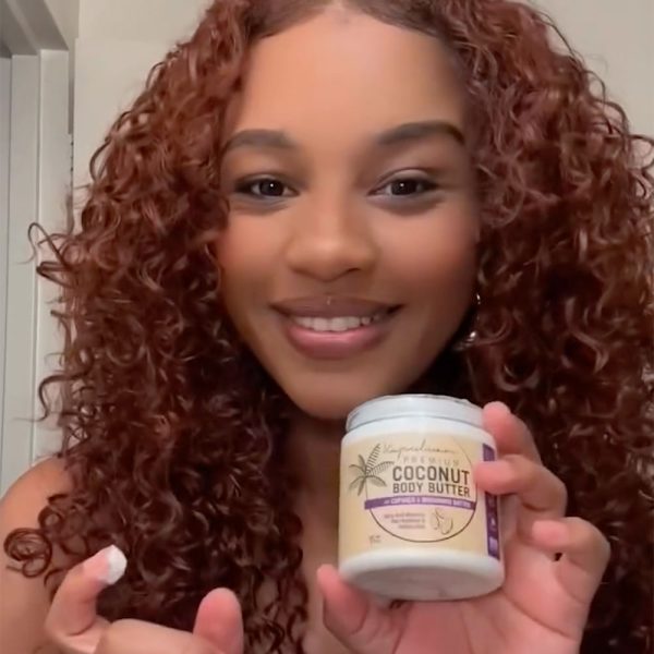 A curly-haired person smiles while holding a jar of Body Butter w/ Cupuaçu & Murumuru. The label is partially visible, and the setting appears to be indoors.