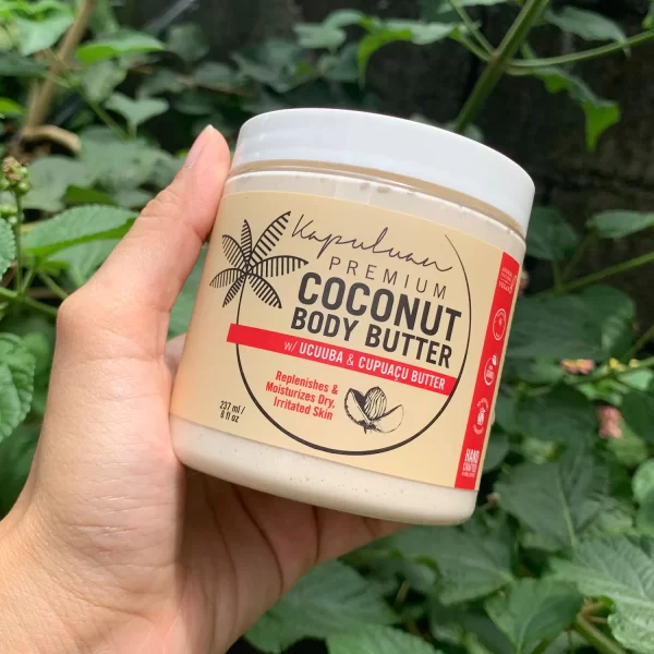 A person holds a container of Body Butter with Ucuuba & Cupuacu. The label highlights ingredients like Ucuuba and Cupuacu butter, and states it replenishes and moisturizes dry, irritated skin. The container is in front of leafy green plants.