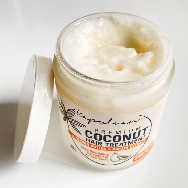 A jar of Coconut Hair Treatment with an open lid, showing the creamy white texture inside, placed on a white surface. the label includes ingredients like mango butter and papaya extract.