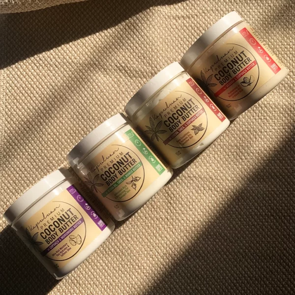 Four containers of Body Butter with Ucuuba & Cupuacu are arranged in a diagonal row on a textured surface with sunlight casting shadows. Each container has a distinct color label, indicating different variants of the body butter.
