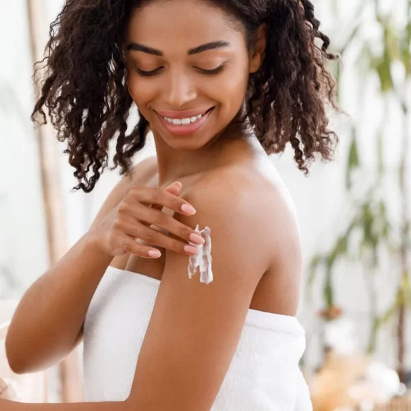 A smiling woman applying Coconut Moisturizing Daily Cream to her shoulder, creating a moment of self-care.