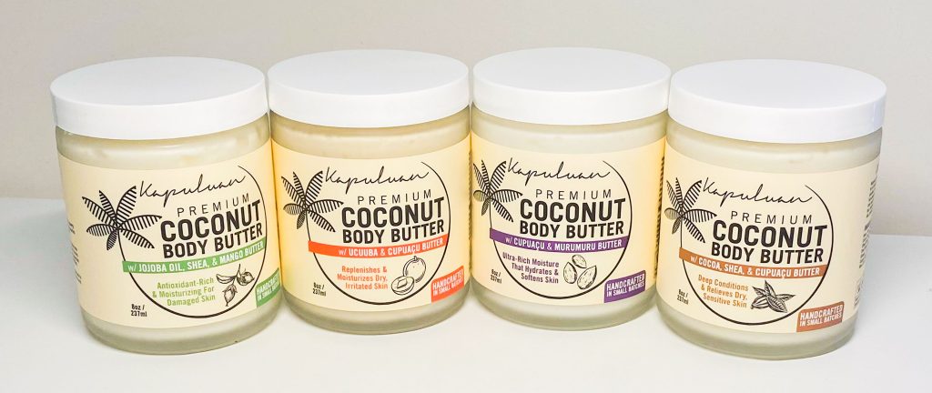 Four jars of premium coconut body butter on a shelf, each labeled differently: original, vanilla patchouli, lavender chamomile, and ginger & cupuacu butter.