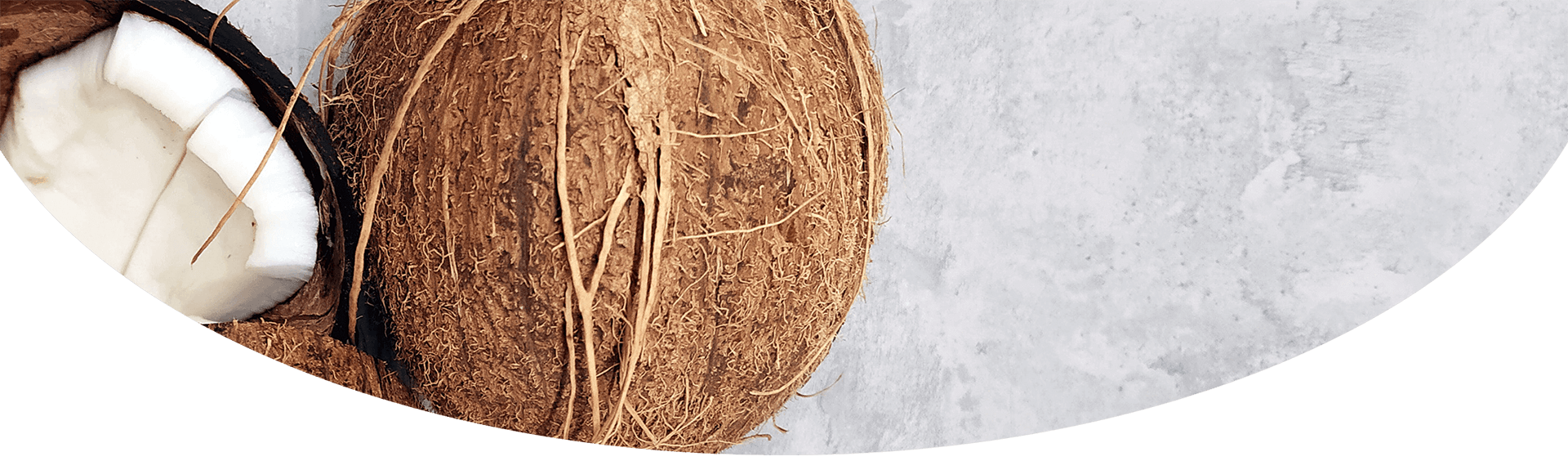 A close-up image featuring a whole coconut, a few coconut pieces, and a jar of coconut oil on a textured white surface, highlighting the fibrous brown exterior and the white flesh inside.