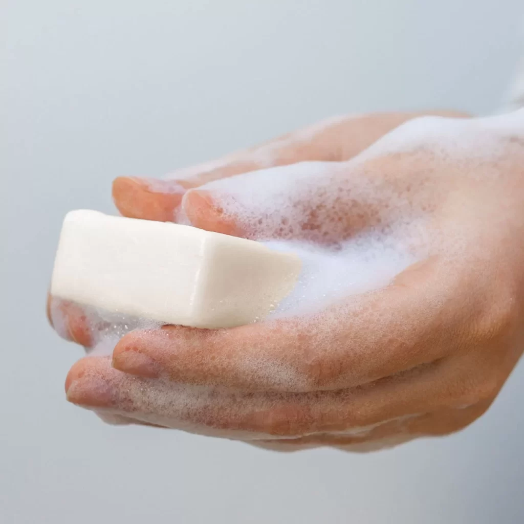 A pair of hands lathering up with a Coconut Oil Soap with Hydrating Cocoa Butter, promoting cleanliness and hygiene.