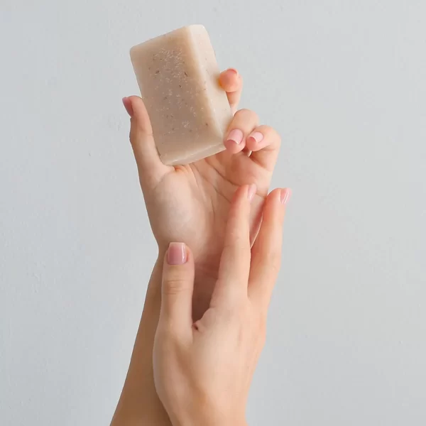 A hand holding a translucent Coconut Oil Soap with Exfoliating Oatmeal against a plain background, showcasing a simple and clean aesthetic.
