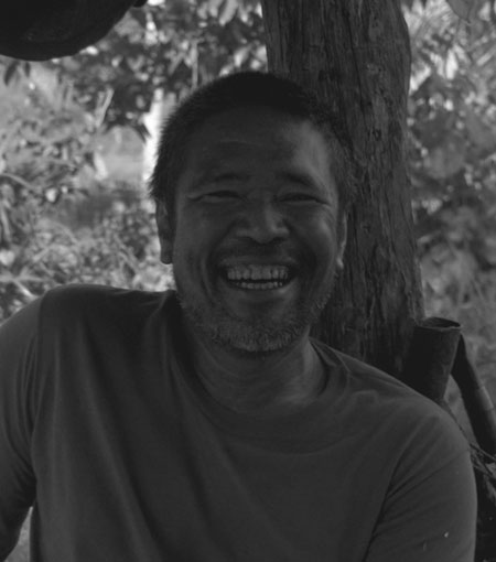 A black and coconut white photo capturing the genuine smile of a man enjoying a moment outdoors, with the hint of nature's backdrop softly blurred in the background.