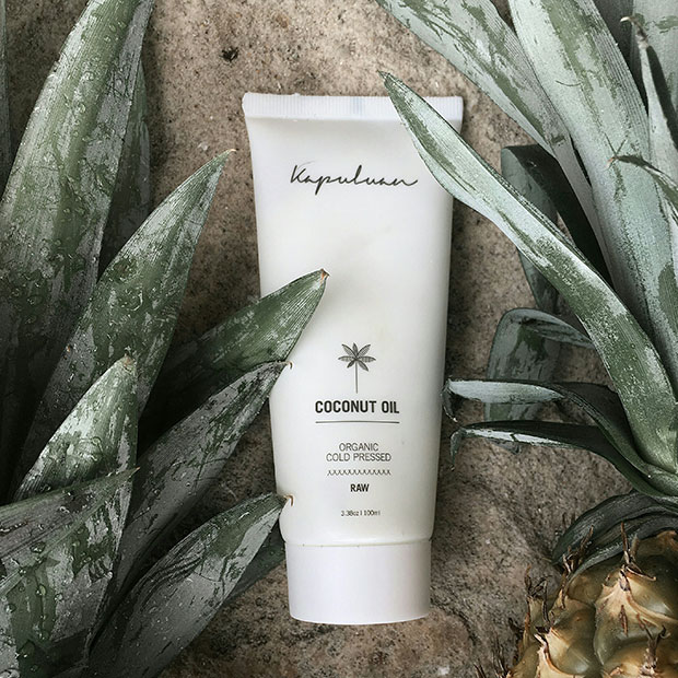 A tube of organic cold-pressed coconut oil by Kapuluan, placed amidst green succulent leaves, evoking a natural and coconut-friendly vibe.
