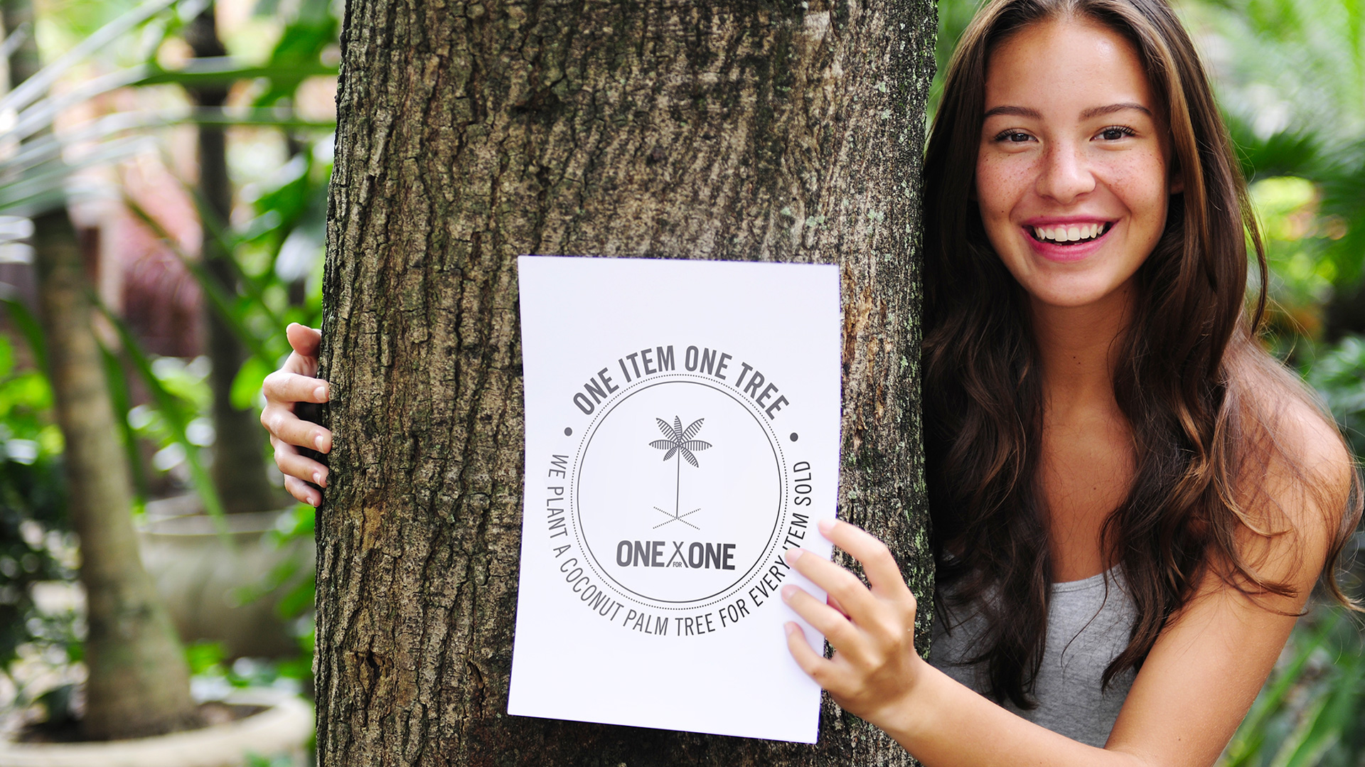 A smiling young woman holding a sign promoting an eco-friendly initiative, "one item one tree," pledging to plant a coconut tree for every product sold.