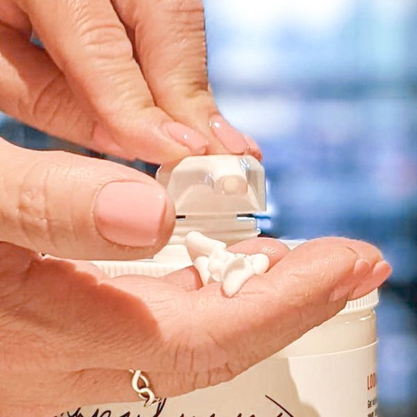 Close-up of a person's hands dispensing Coconut Moisturizing Daily Cream from a pump bottle into their palm, with a blurred background.