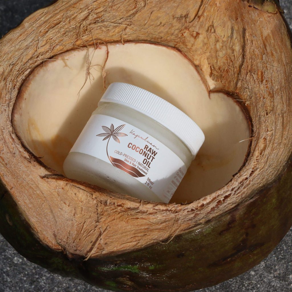 A jar of coconut oil nestled in a freshly cut open coconut, placed on a concrete surface, emphasizing natural ingredients.