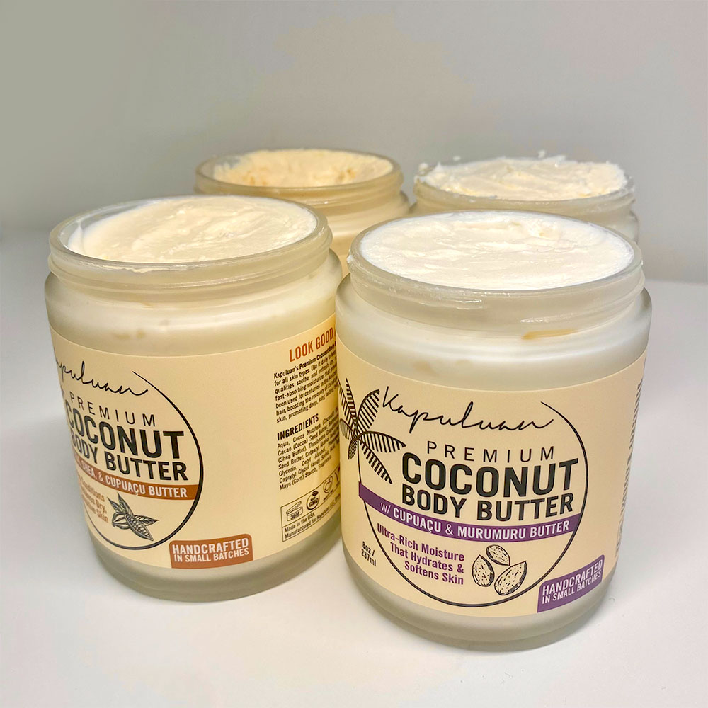 Four containers of premium coconut body butter on a white surface. the labels mention ingredients like murumuru and cupuaçu butter.