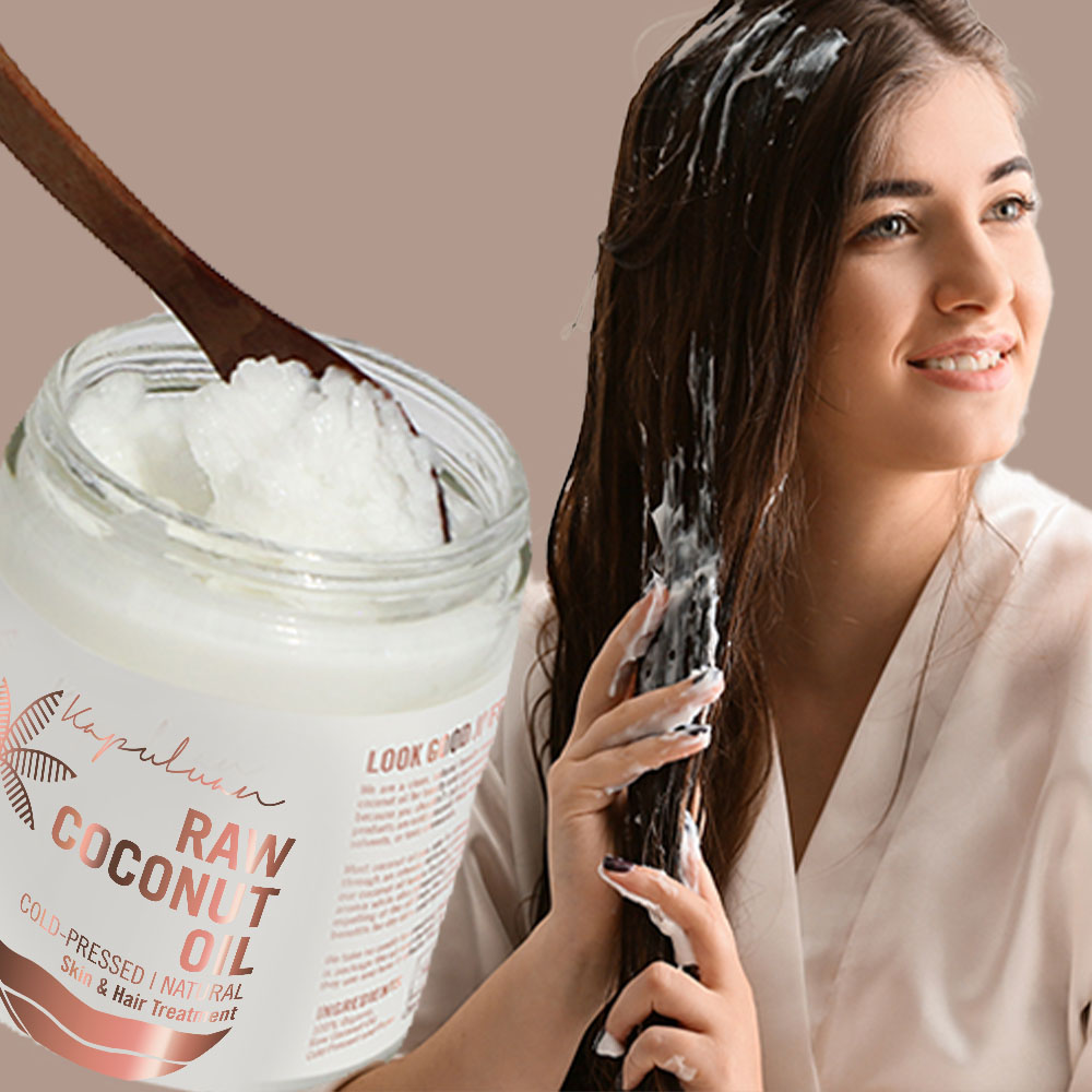 A smiling woman applies coconut oil to her hair, holding a jar labeled "raw coconut oil" next to her. the image highlights the use of natural products for hair care.