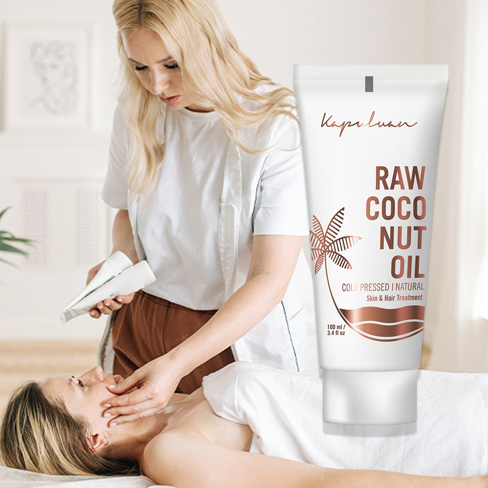 A woman massages another woman's head in a serene spa setting, with a bottle of 'raw coconut oil' displayed in the foreground.