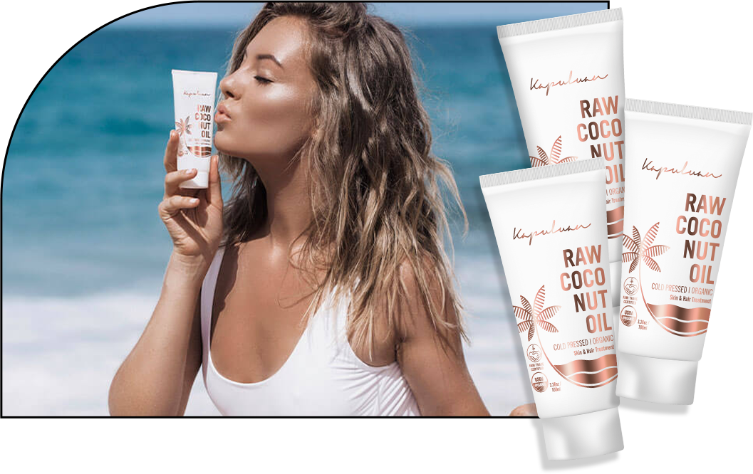A woman on a beach applies coconut oil skincare product from a tube. the image also shows multiple similar product tubes with "raw coconut oil" labels.