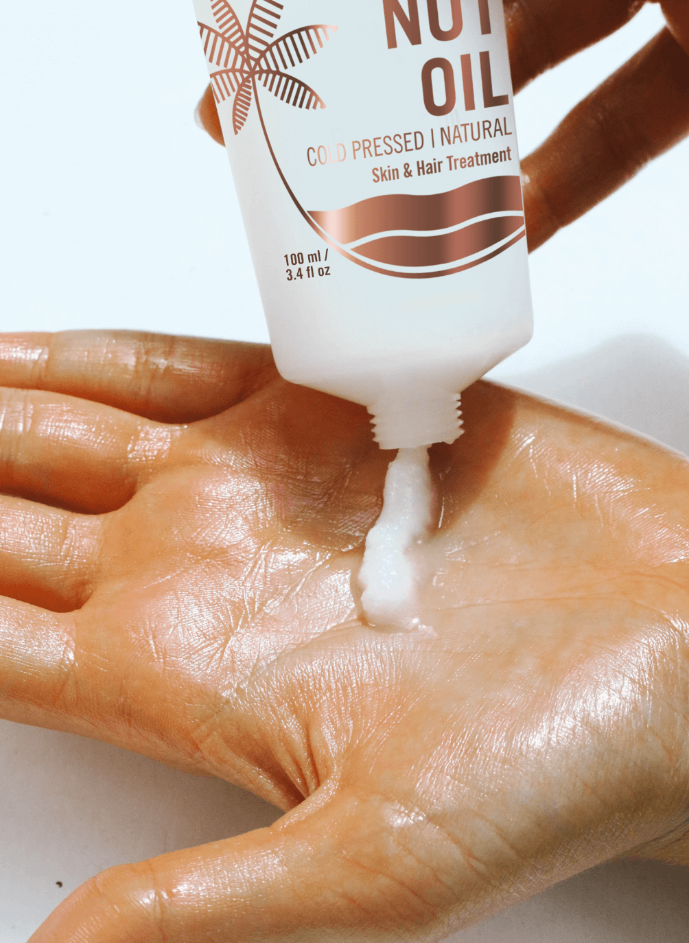 A person's hand with a small amount of coconut oil being dispensed from a bottle labeled "coconut oil. cold pressed natural skin & hair treatment.
