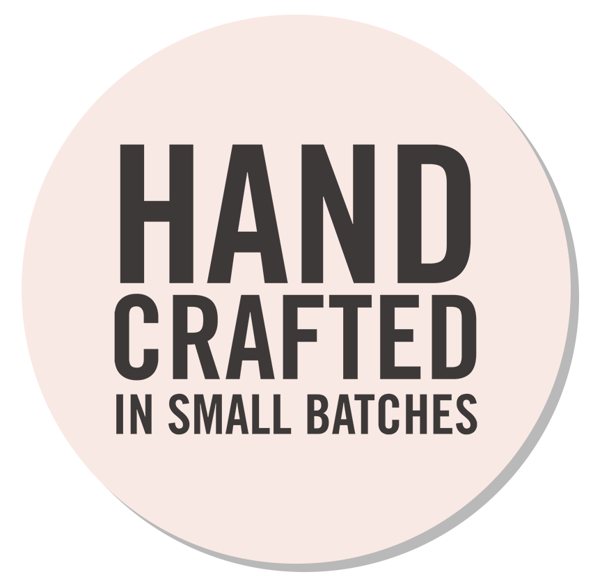 A round, minimalist badge with a black border on a pale pink background, featuring the text "hand crafted in small batches" in black, stylized font.