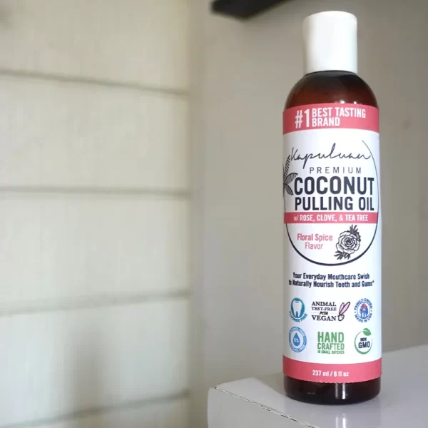 A bottle of Coconut Pulling Oil - Floral Spice is displayed. The label highlights that the product is handcrafted, vegan, non-GMO, and made by a woman-owned company. It is USDA certified organic and meant for oral health.
