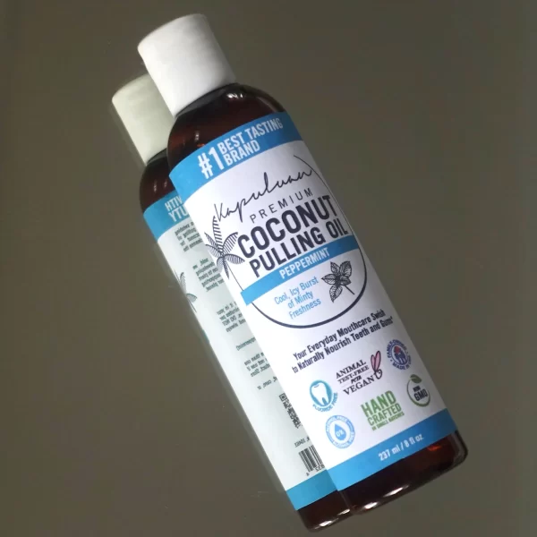 Two bottles of Coconut Pulling Oil - Peppermint lie on a reflective surface. The label highlights that it is the "#1 Best Tasting Brand" and includes badges for being natural, vegan, and hand-crafted in small batches.